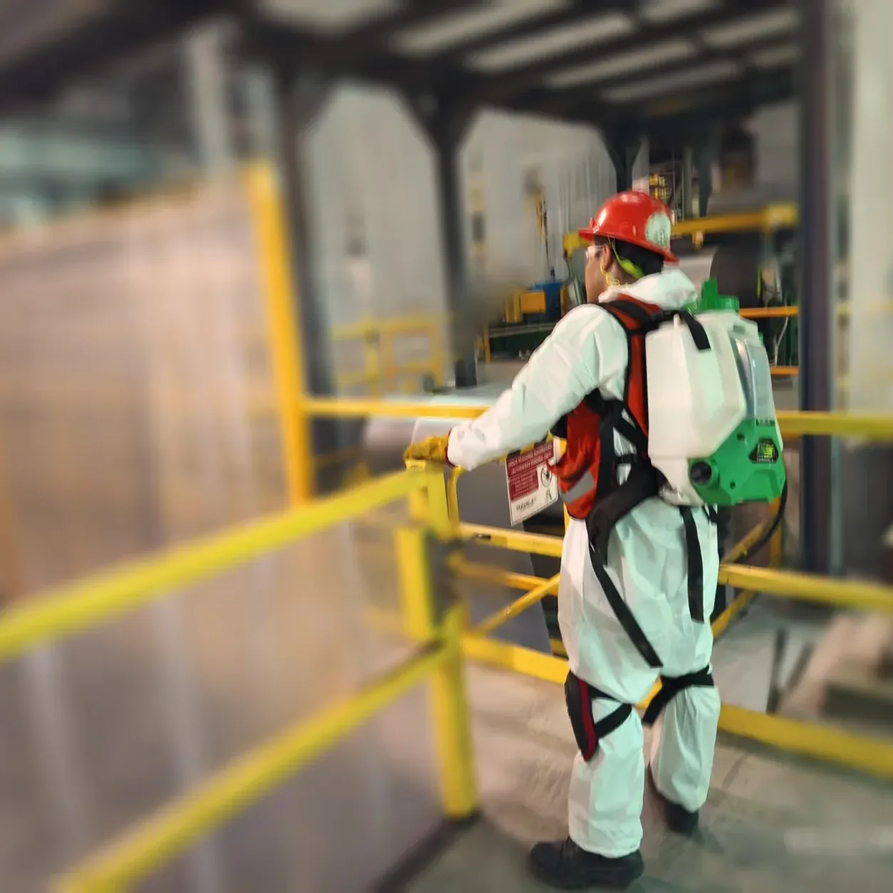 Técnico con traje de protección de espaldas junto a barandales amarillos