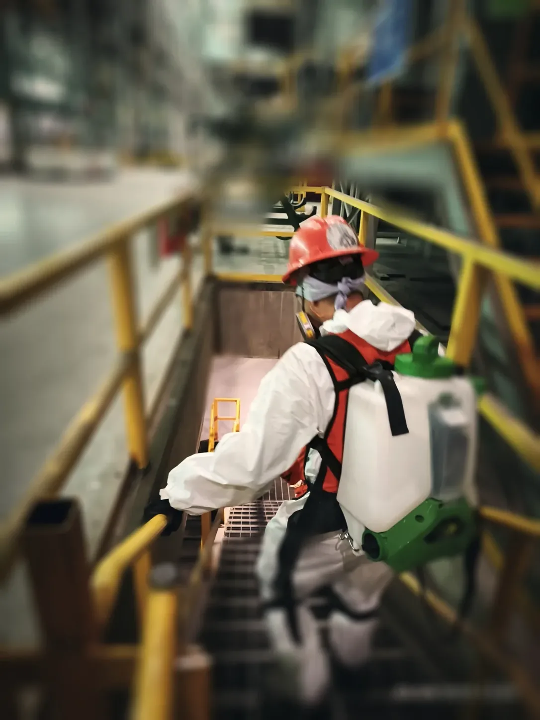 Técnico con traje blanco y aspersor bajando una escalera de planta